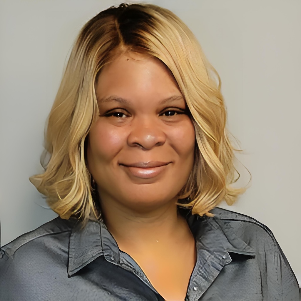 Portrait of a woman with shoulder-length blonde hair, wearing a gray satin blouse, smiling against a neutral background.
