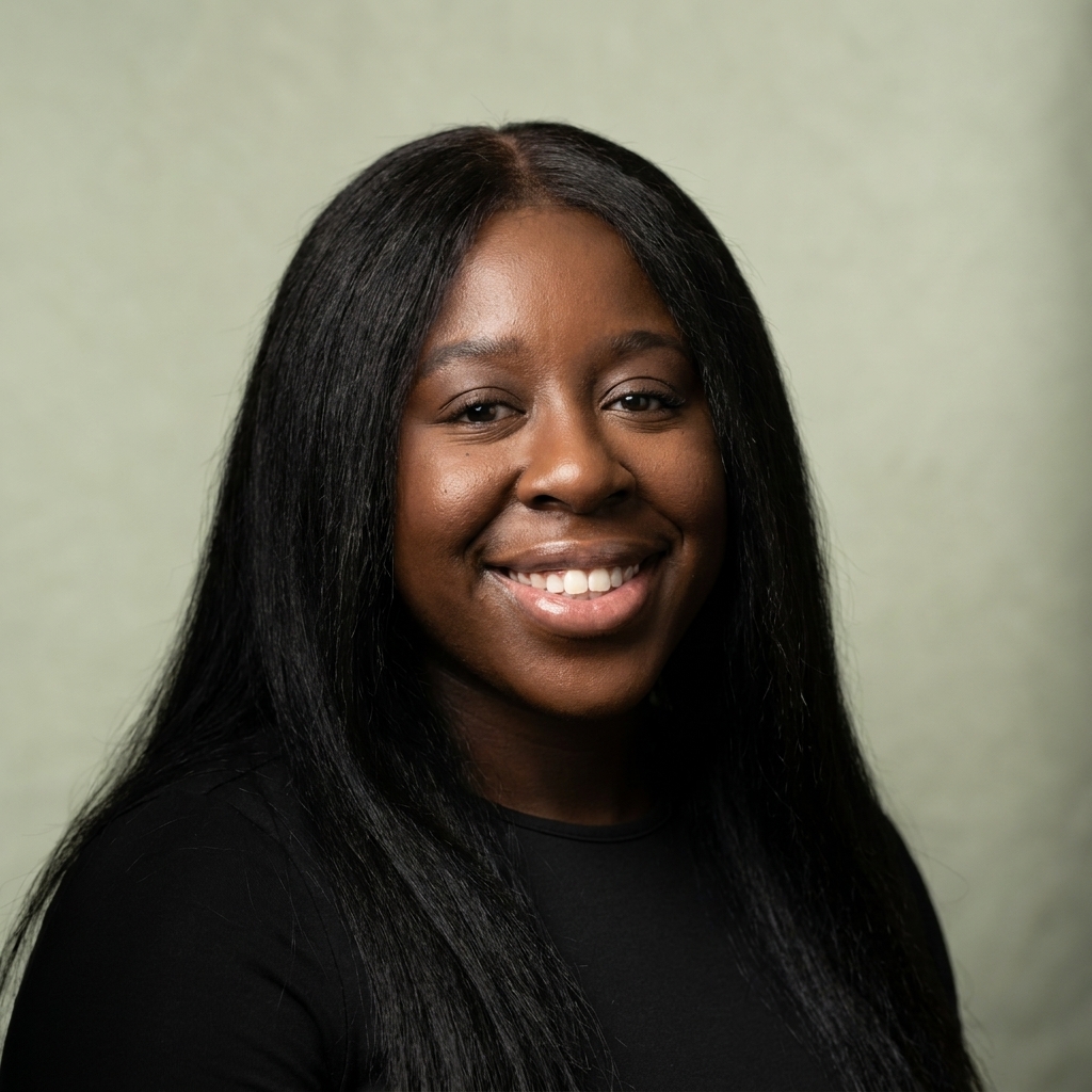 Smiling Black woman with long black hair wearing a black top against a neutral greenish background.