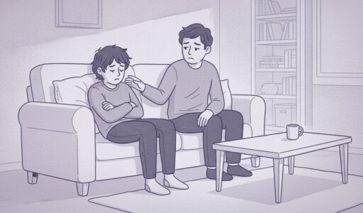 An upset teenage boy sits at home on his couch. His dad sits next to him and looks worried.